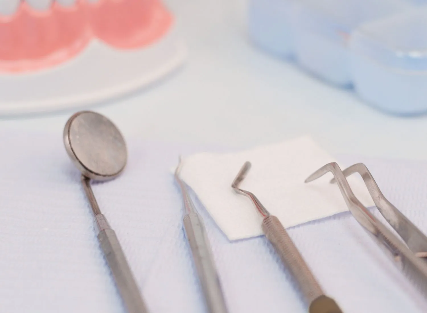 Close-up of dental tools including mirror, scaler, and tweezers on a white cloth.