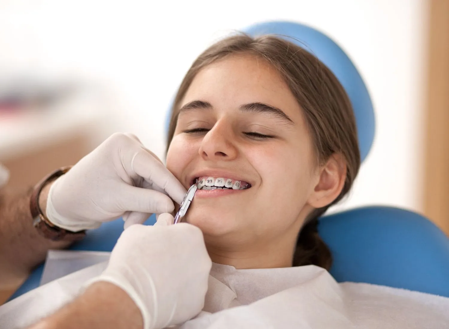 Dentist adjusting braces on a smiling teenage girl reclining in a dental chair.