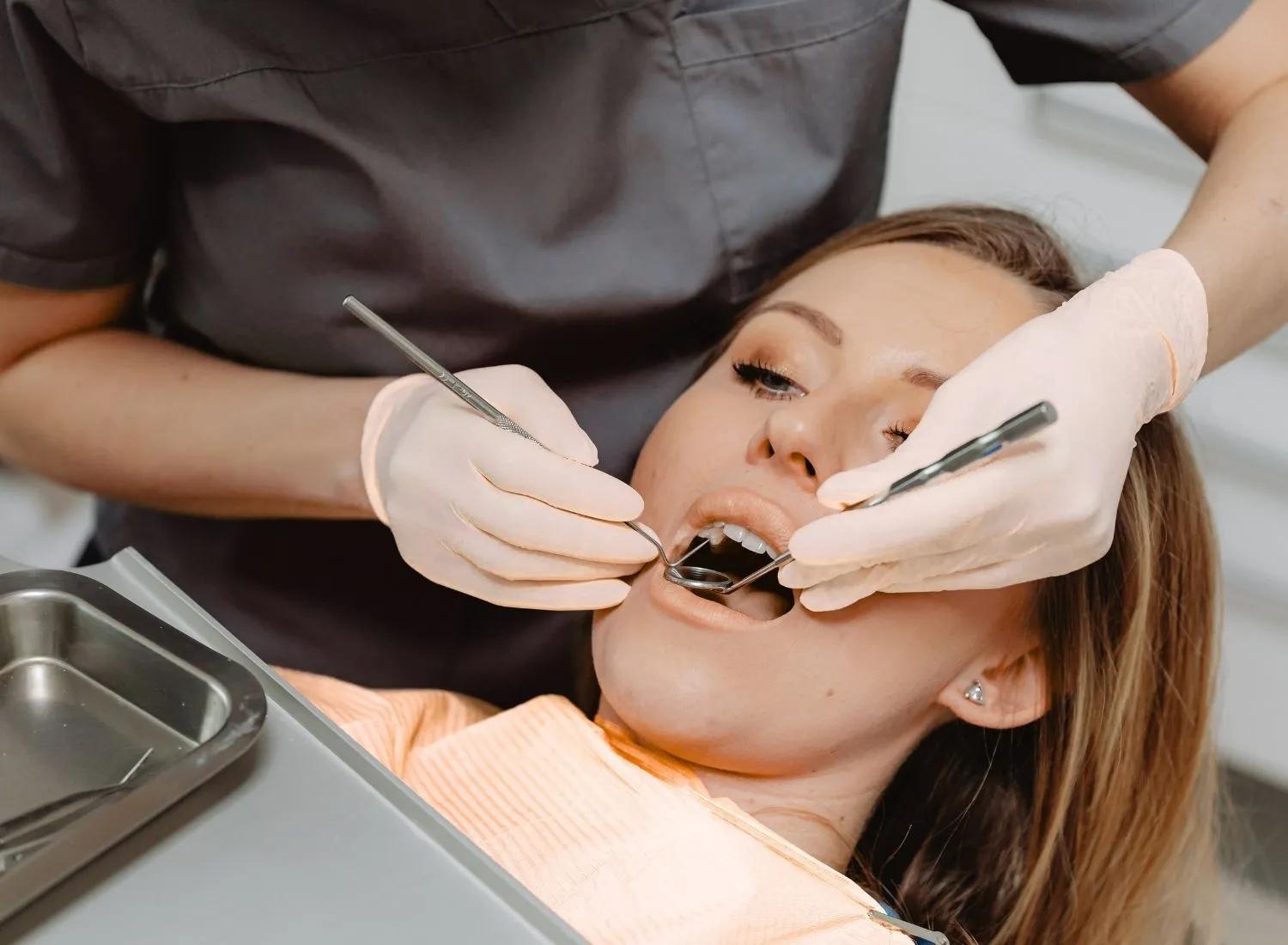 Dentist in gloves examining a woman's open mouth using dental tools in a clinic.