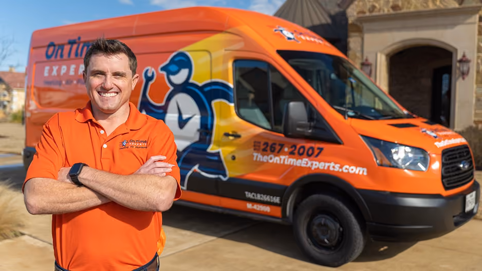 Man in orange polo stands with arms crossed in front of an orange service van with company branding.