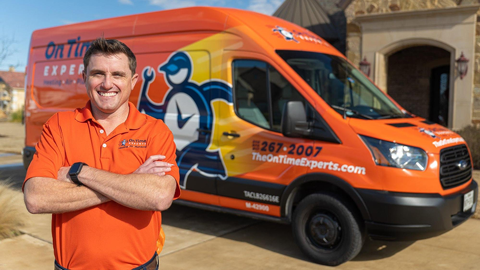 Man in orange polo stands with arms crossed in front of an orange service van with company branding.