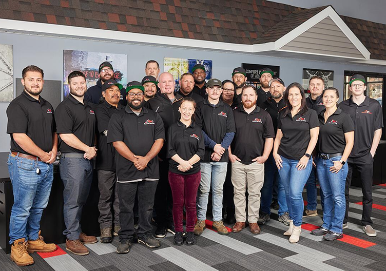 Group of men and women in matching black polo shirts posing indoors on patterned carpet.