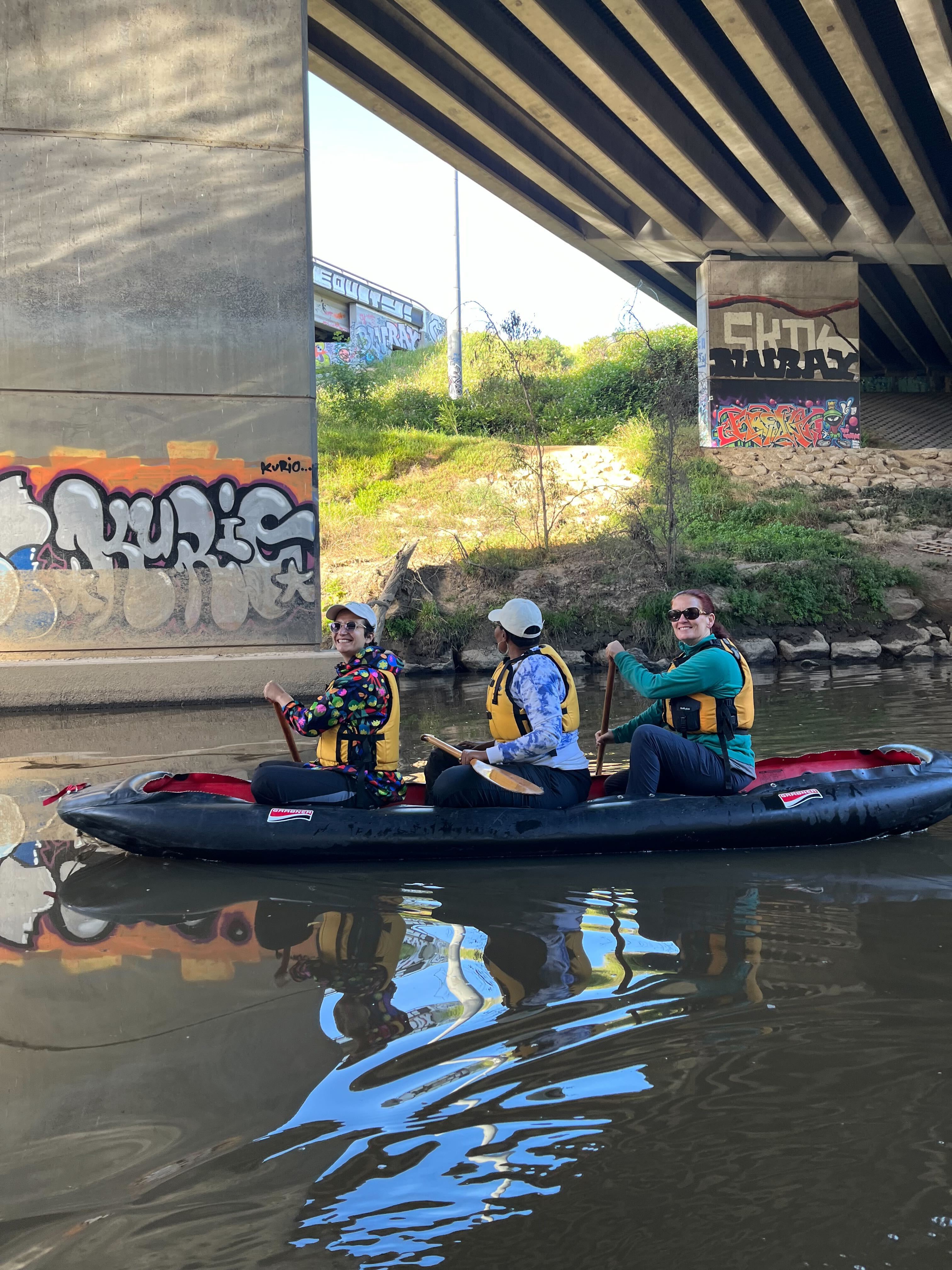 Three people kayaking on the Birrarung River under a bridge