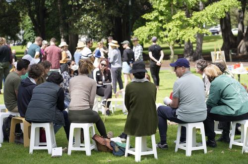 Community members seated on stools in small groups at a Regen Melbourne outdoor event