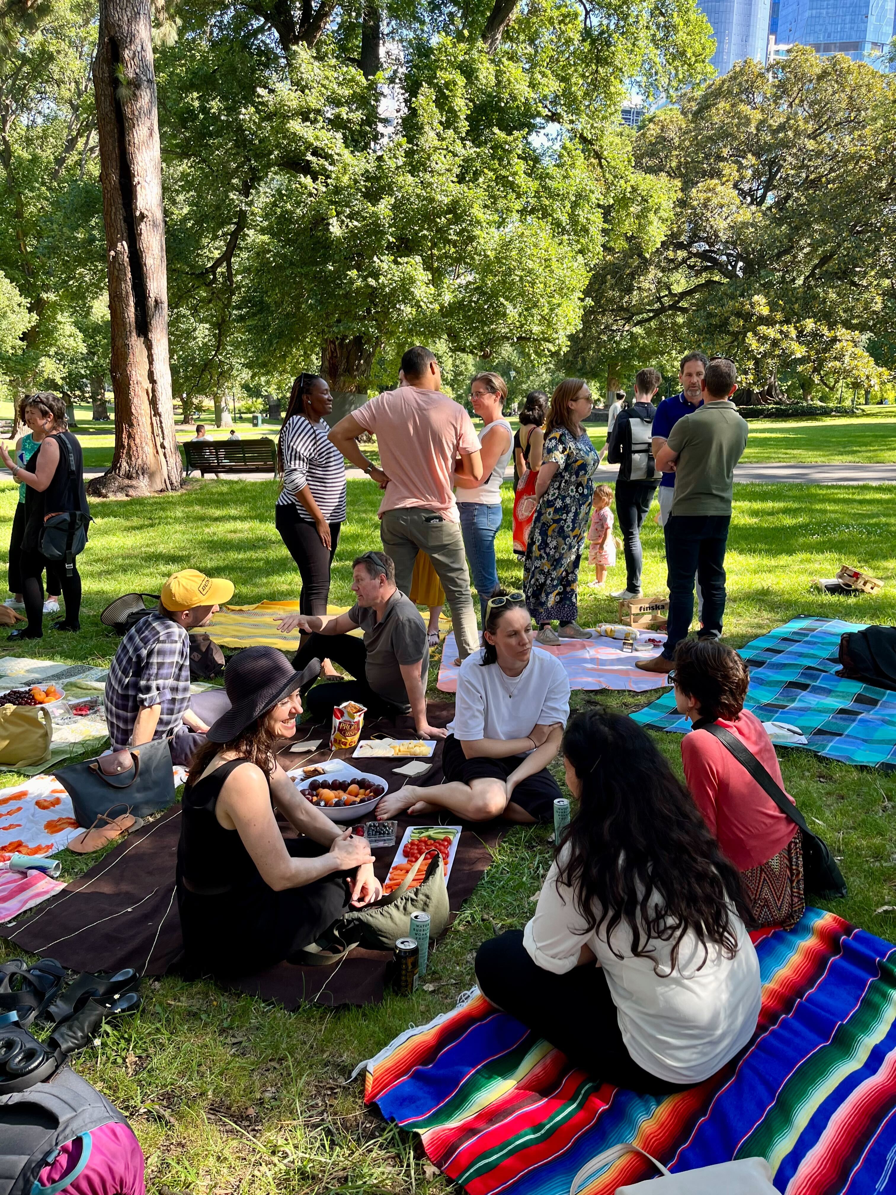 Community members sharing food on colourful blankets at a park picnic