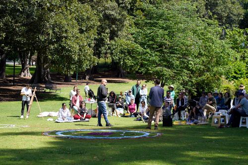 Wide view of a community gathering in a Melbourne park with circular ground art and picnic blankets