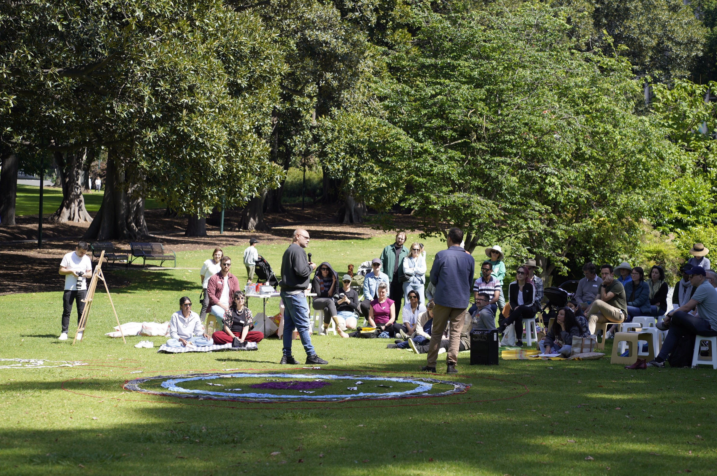 Wide view of a community gathering in a Melbourne park with circular ground art and picnic blankets