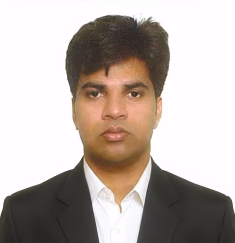 Portrait of a man with dark hair wearing a black suit jacket and white collared shirt against a plain white background.