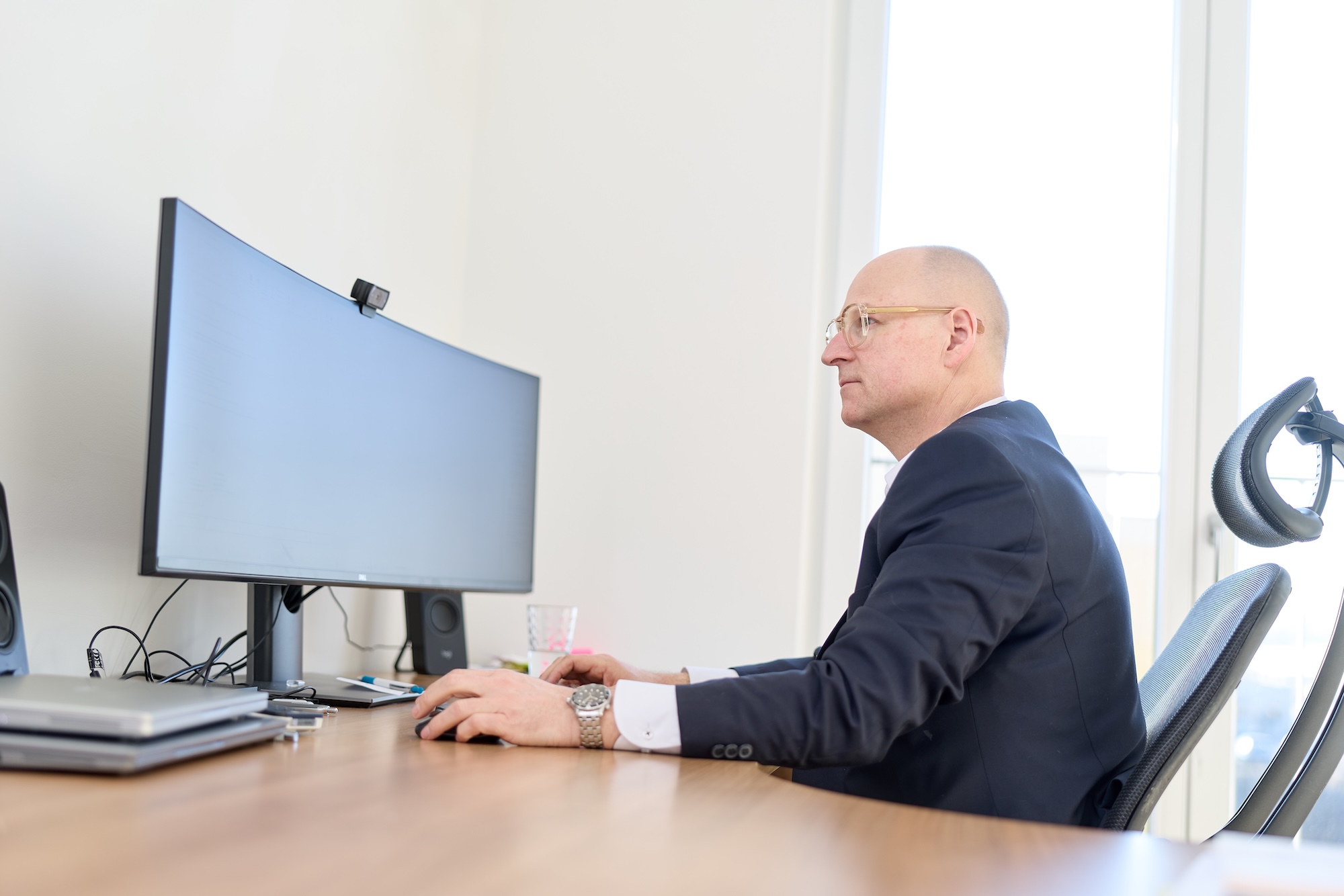 Mann sitzt seitlich am Schreibtisch und arbeitet am Monitor