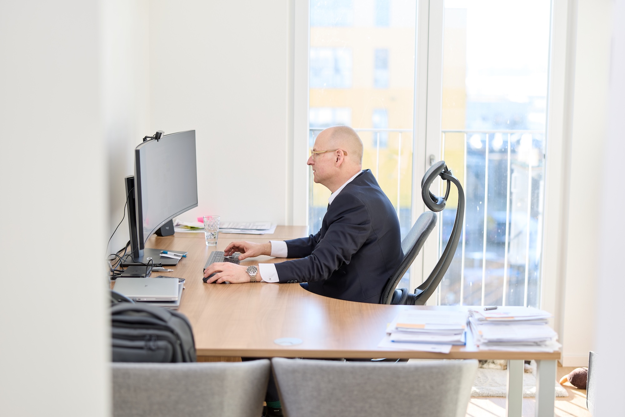 Mann sitzt im hellen Büro an einem Schreibtisch aus größerer Distanz