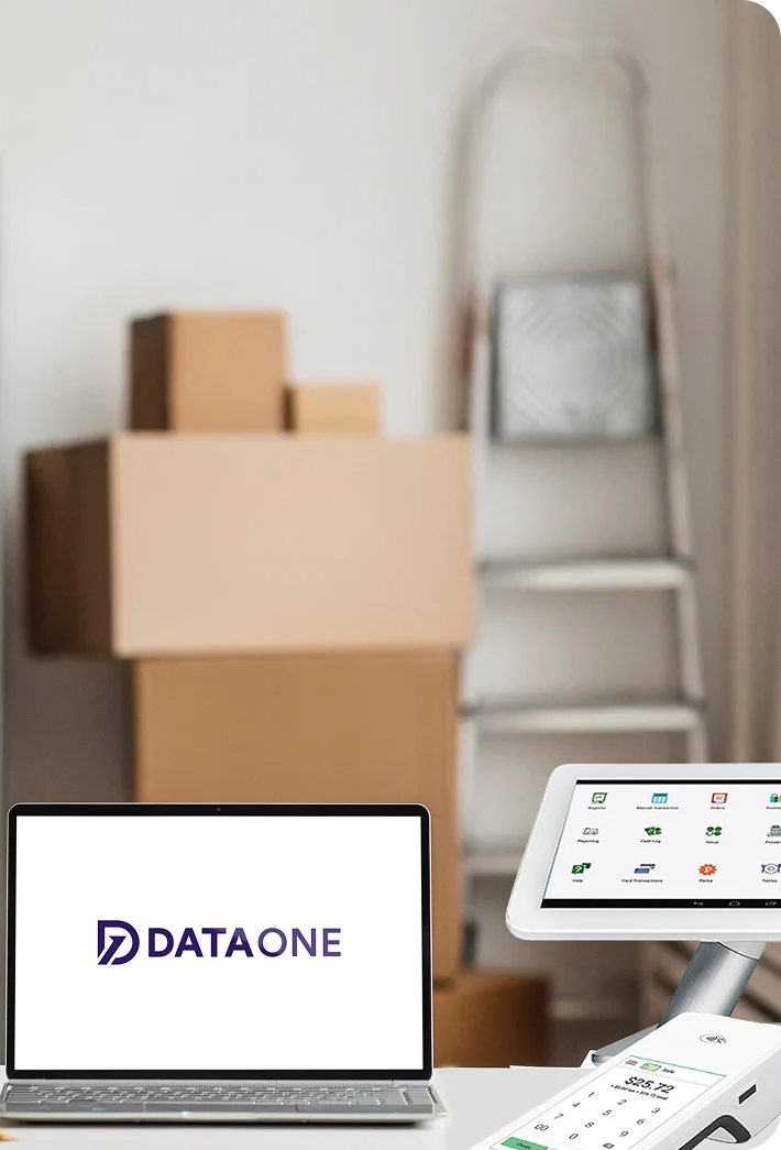 Laptop displaying DATAONE logo beside a digital payment terminal and tablets with blurred moving boxes and ladder in the background.