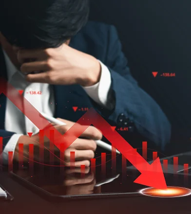 Stressed man in a suit rubbing his forehead with red downward trending financial charts overlay.