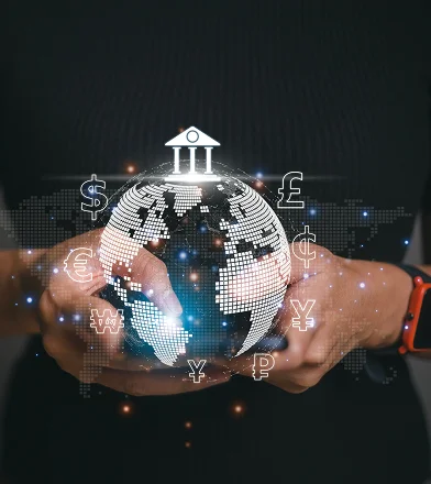 Hands holding a digital globe with floating international currency symbols and a bank icon above it.
