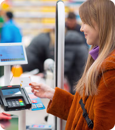 Woman in orange coat using a contactless card to make a payment at a point-of-sale terminal.