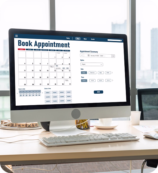 Desktop computer on office desk displaying a book appointment calendar interface with date and time selection options.