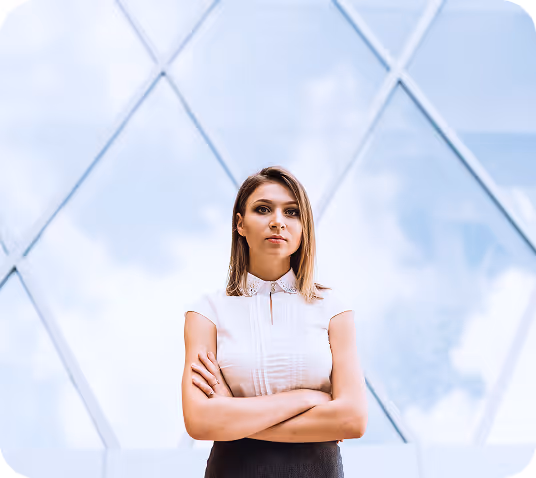 Confident woman standing with arms crossed in front of a modern glass building reflecting the sky.
