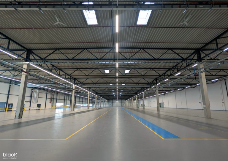 Spacious, empty industrial warehouse interior with high ceiling, metal beams, and marked concrete floor.