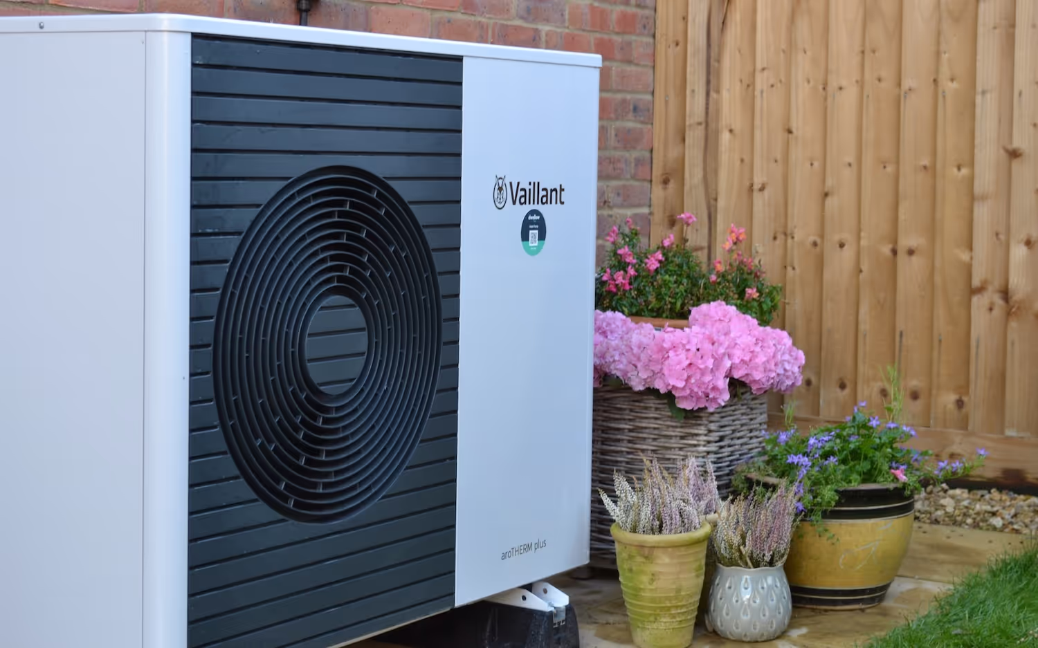 Vaillant aroTHERM plus heat pump installed in a garden. The heat pump has a dwellow sticker on the front.