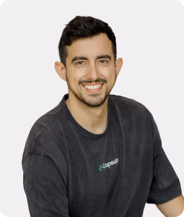 Smiling man with short dark hair and beard wearing a dark Capsule-branded t-shirt.
