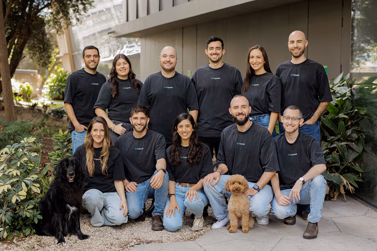 Group of eleven people wearing black Capsule shirts and two dogs posing outdoors in front of a building.