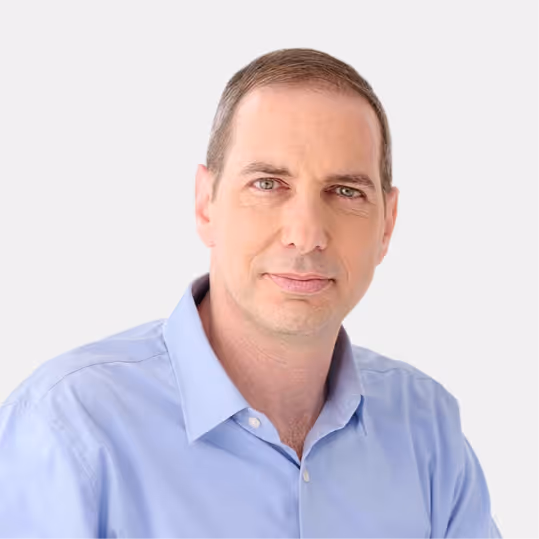 Portrait of a man with short brown hair wearing a light blue button-up shirt against a white background.