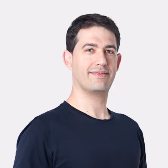 Man with short dark hair wearing a black t-shirt against a plain light background.