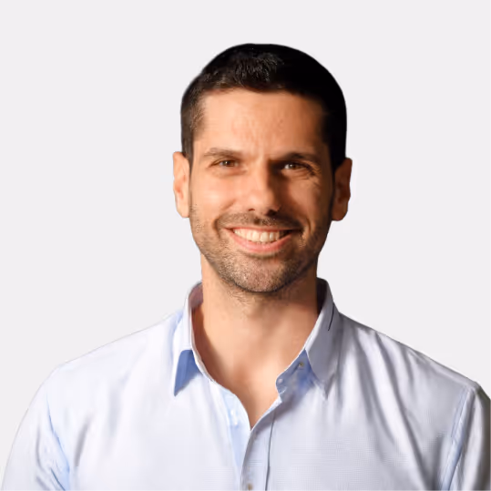 Smiling man with short dark hair wearing a light blue collared shirt against a plain light background.