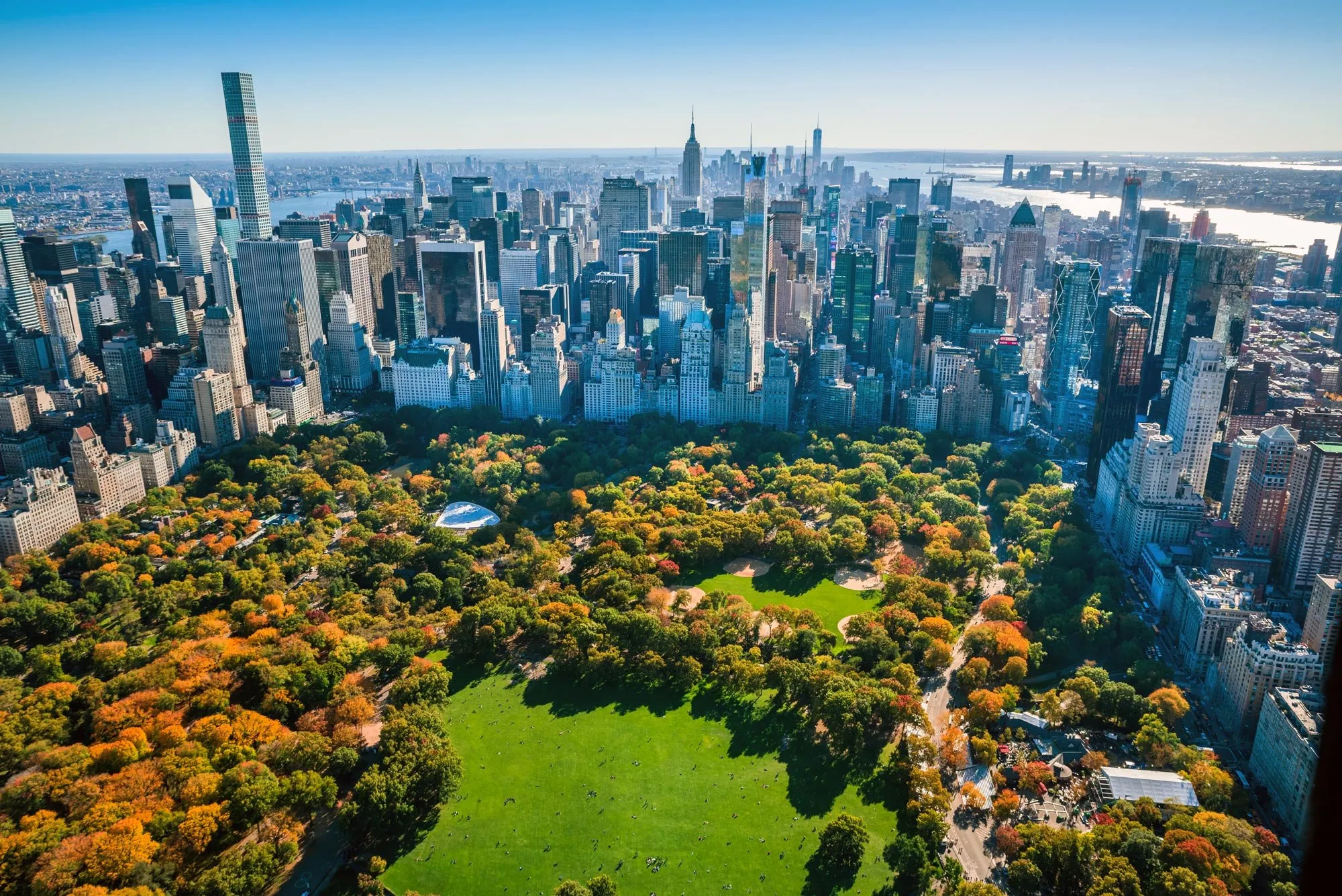 Aerial view of Central Park with autumn foliage and New York City skyscrapers in the background on a clear day.