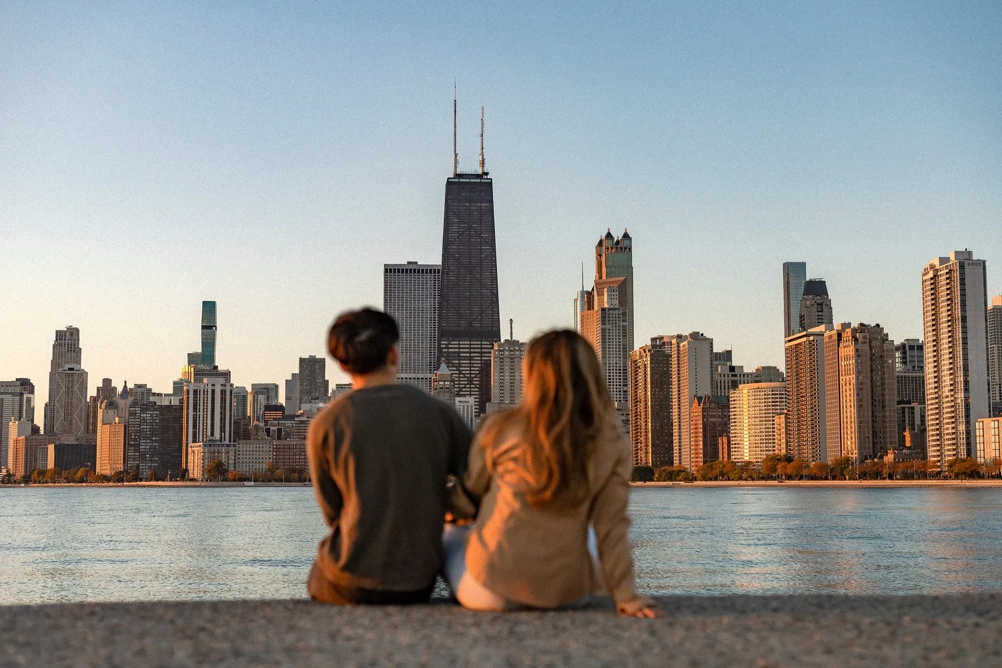 Couple sitting by the water facing the Chicago skyline at sunset.