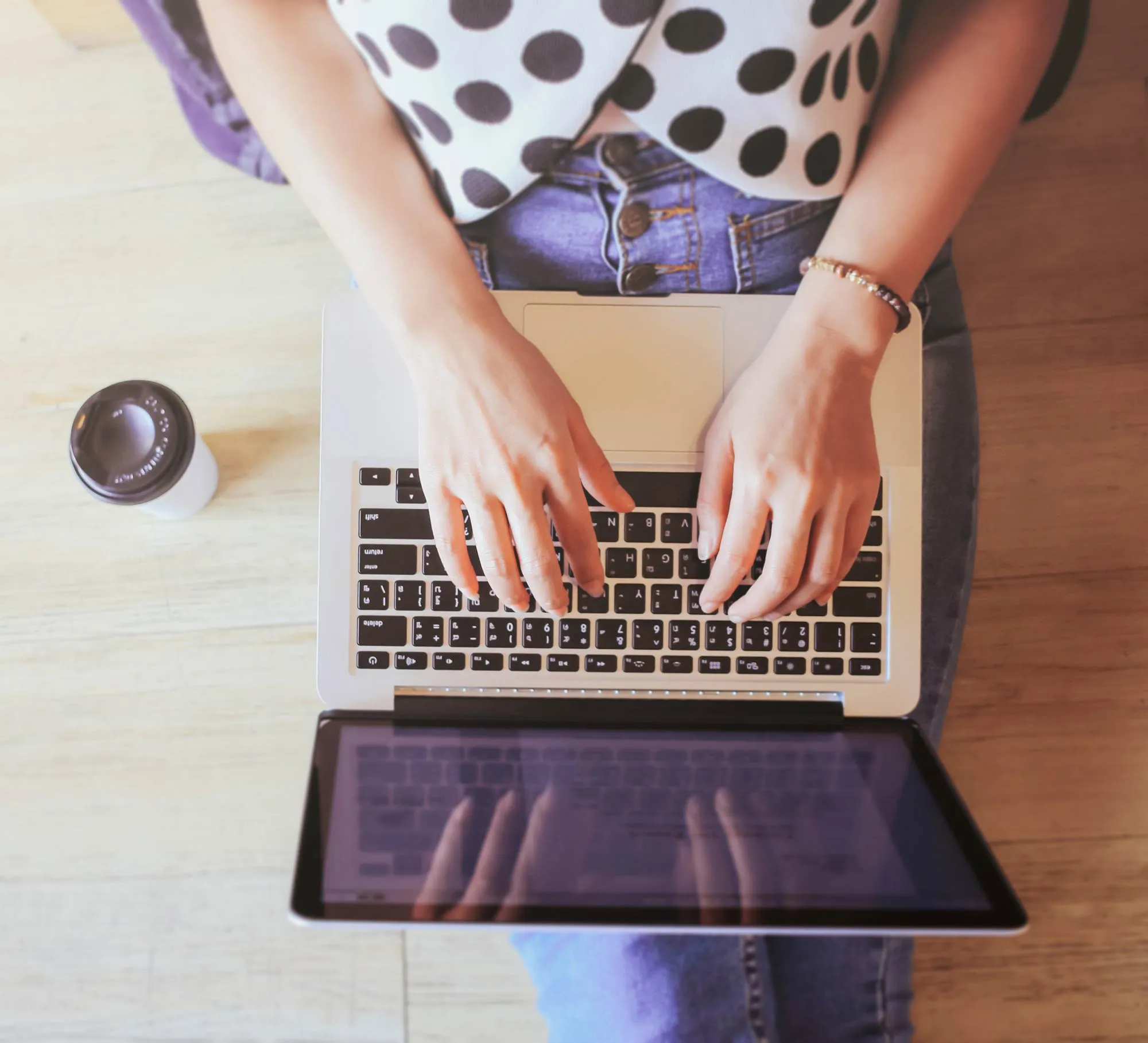 Person typing on a laptop keyboard while sitting with a coffee cup on the table nearby.