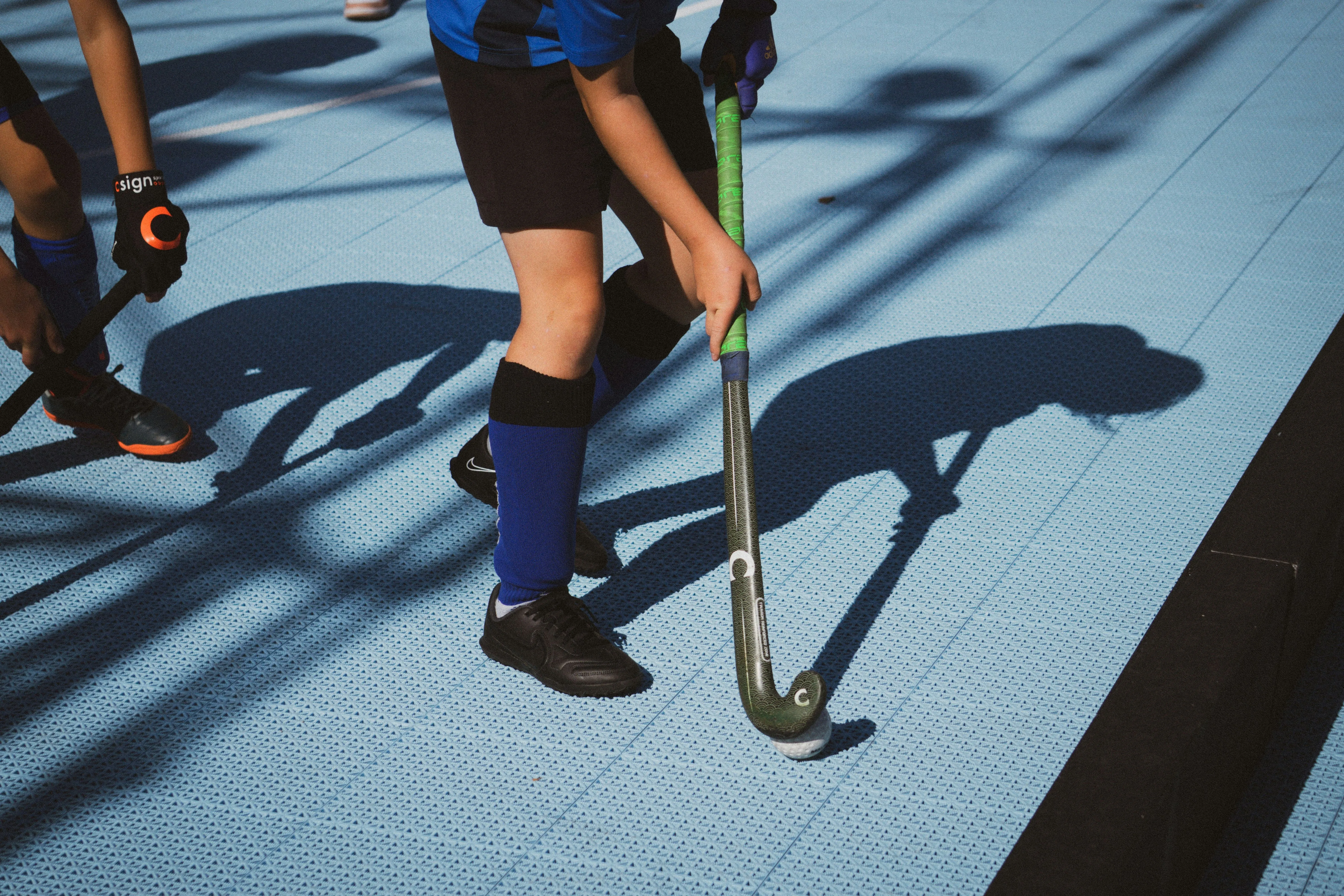 Two players in blue and black sports uniforms playing field hockey on a blue textured surface.