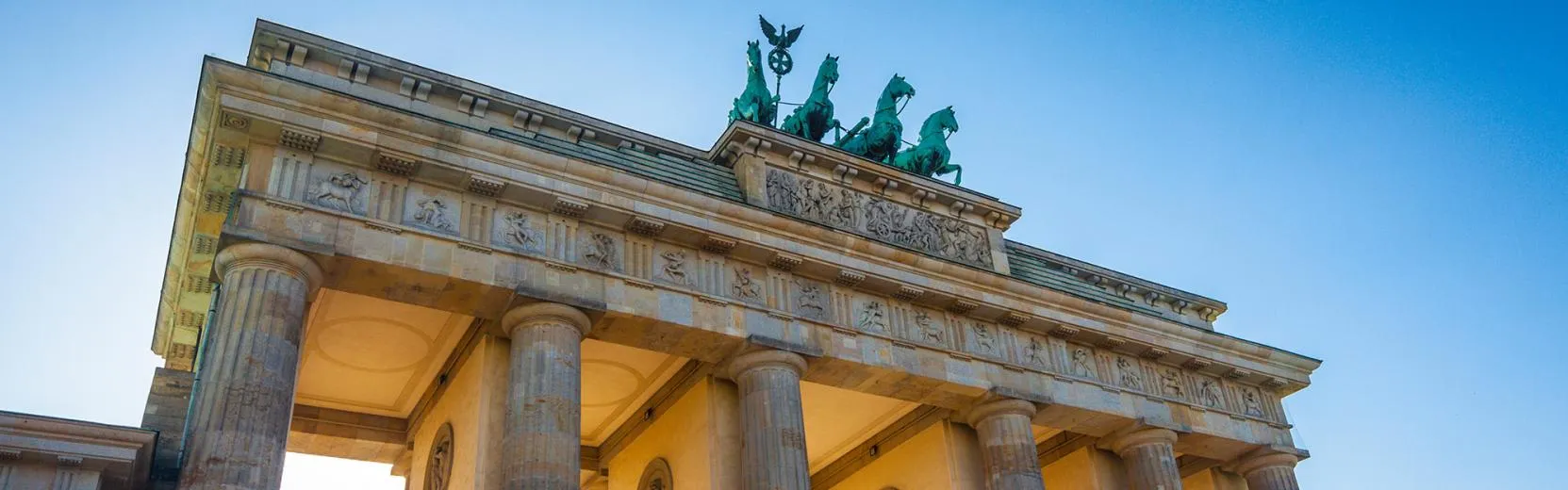 Low-angle view of the Brandenburg Gate in Berlin against a clear blue sky.