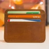 Brown leather cardholder wallet with multiple credit cards inside against a blurred warm-toned background.