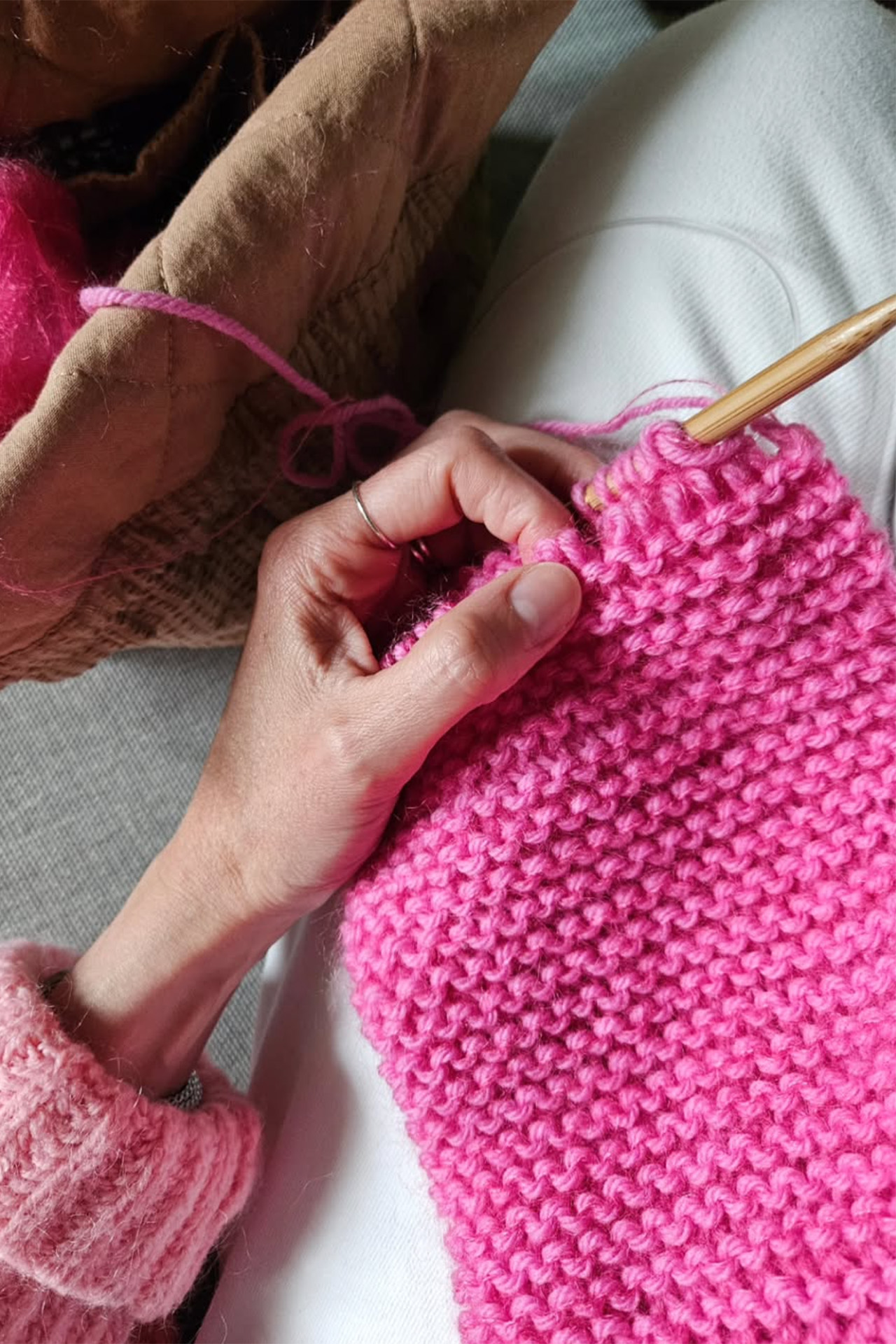 Nahaufnahme einer Hand, die eine Nähnadel in ein gestricktes, flauschiges rosa Kleidungsstück einführt.