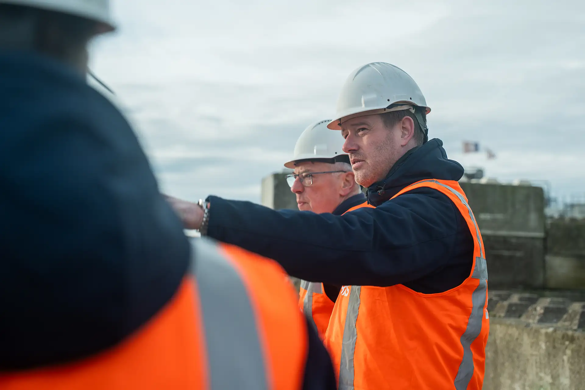 Twee mannen met veiligheidsharnassen en helmen overleggen buiten bij een bouwplaats.