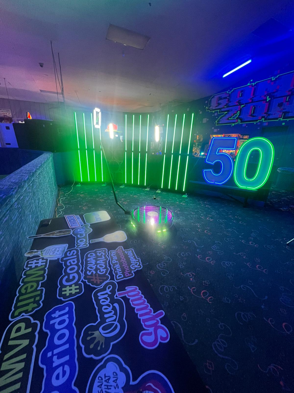 Neon-lit indoor space with colorful carpet, a vertical green LED light panel, a large neon '50' sign, and a floor decorated with social media-style stickers.
