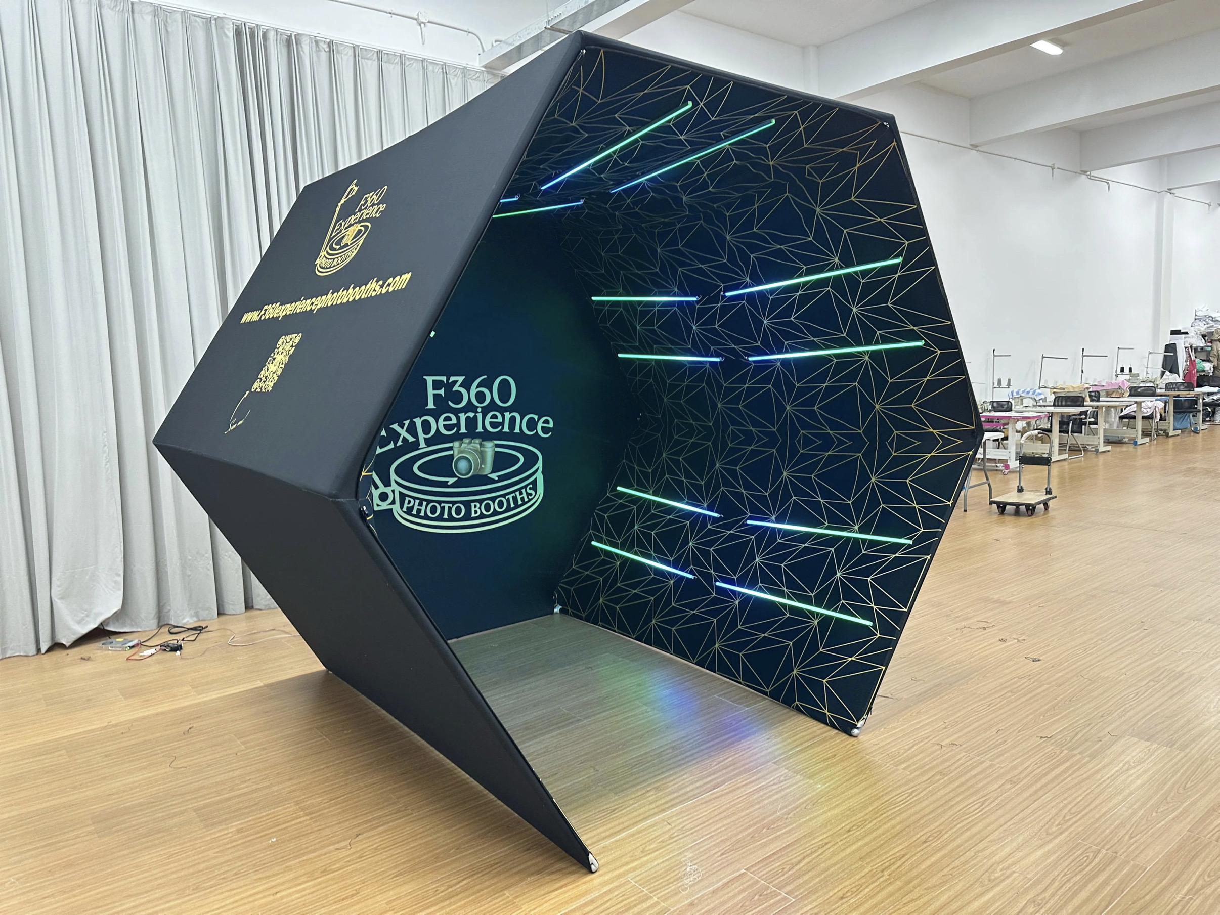 Hexagonal photo booth with geometric patterned interior and horizontal green and blue neon lights, branded with F360 Experience logo.