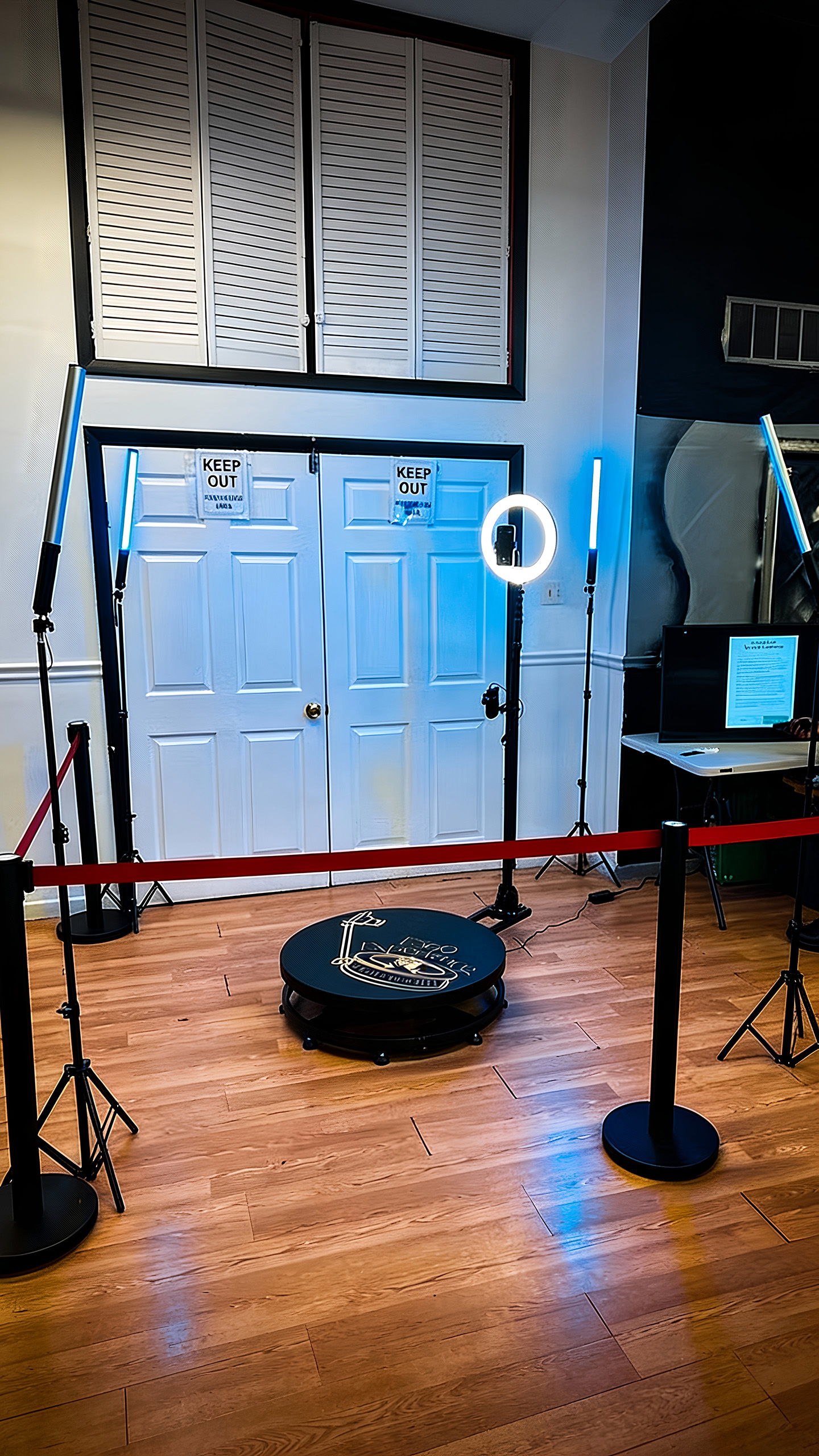 Indoor setup with white double doors surrounded by blue LED light tubes, a circular platform, and a ring light on a wooden floor.