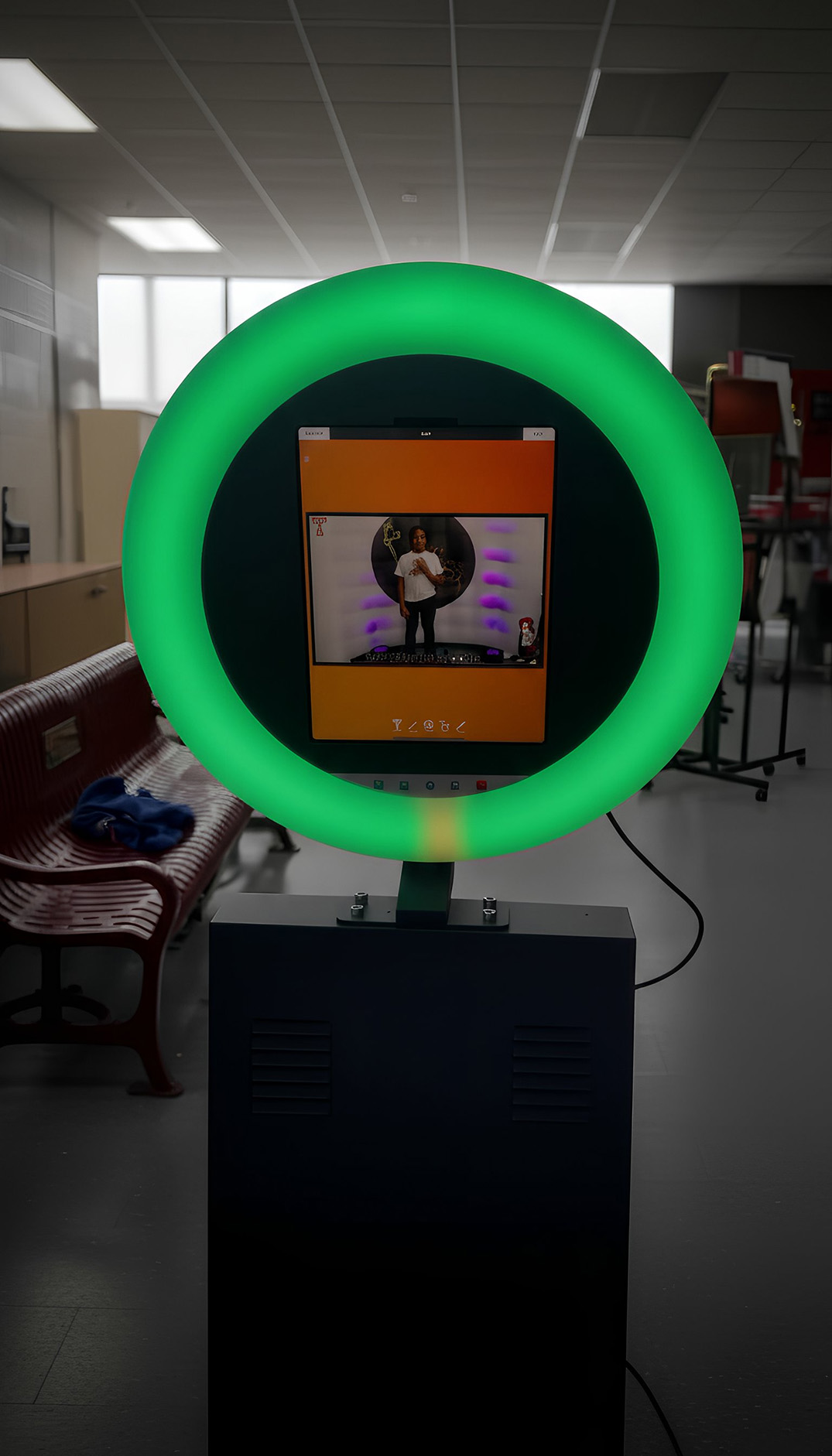 Photobooth with a green LED ring light surrounding a touchscreen displaying a person posing inside the booth.