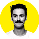 Portrait of a smiling man with dark hair and a mustache on a yellow circular background.