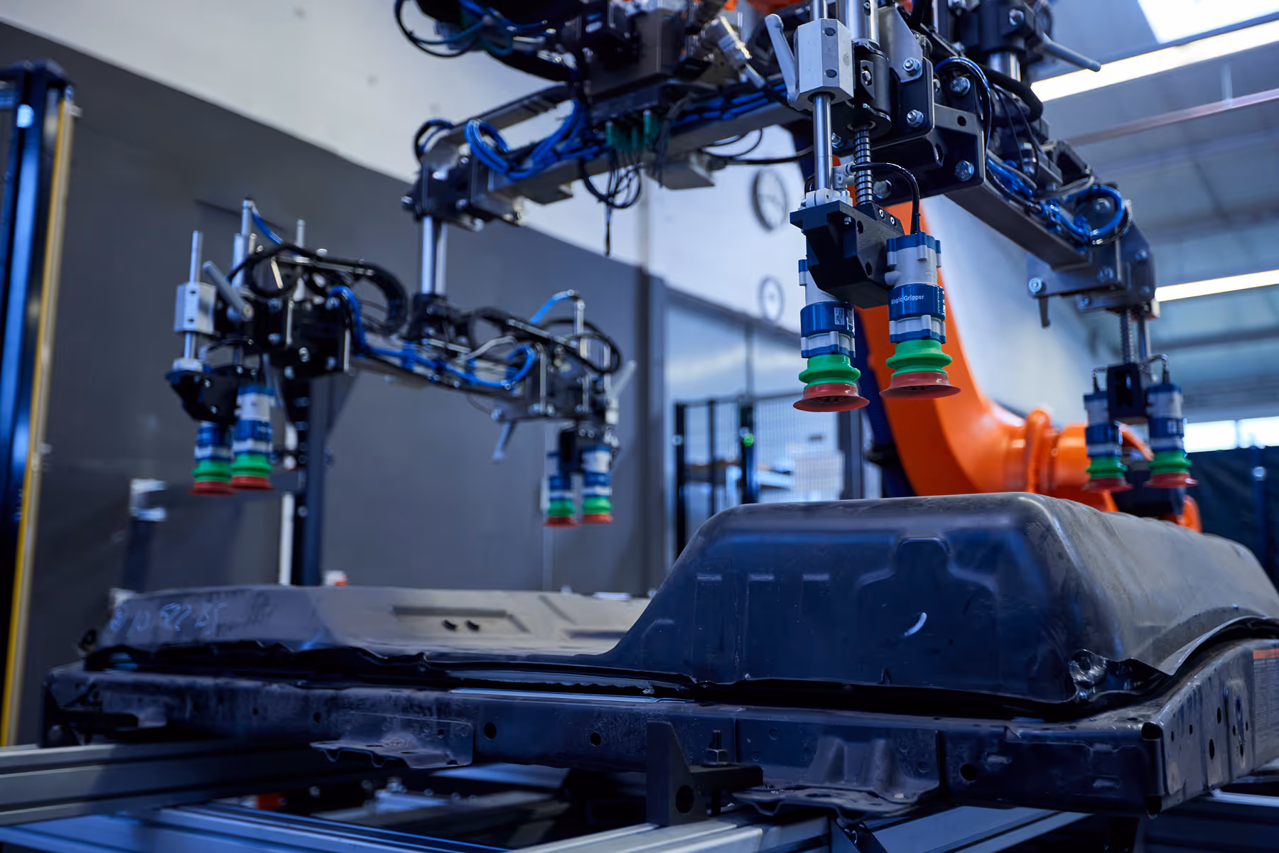 Robotic arms with suction grippers handling a large black industrial component in a factory setting.