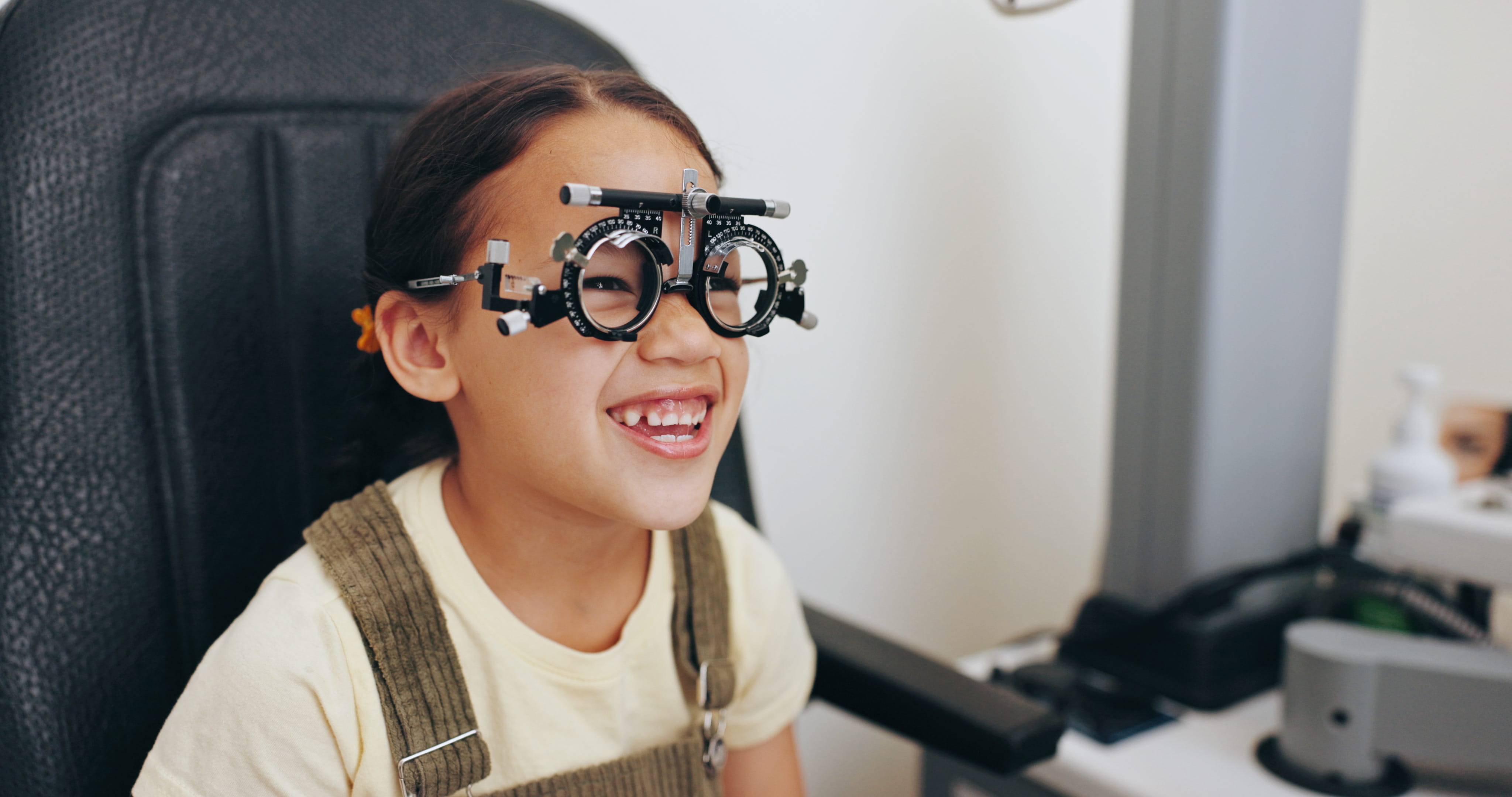 Child smiling during eye exam wearing trial frame glasses at optometrist office