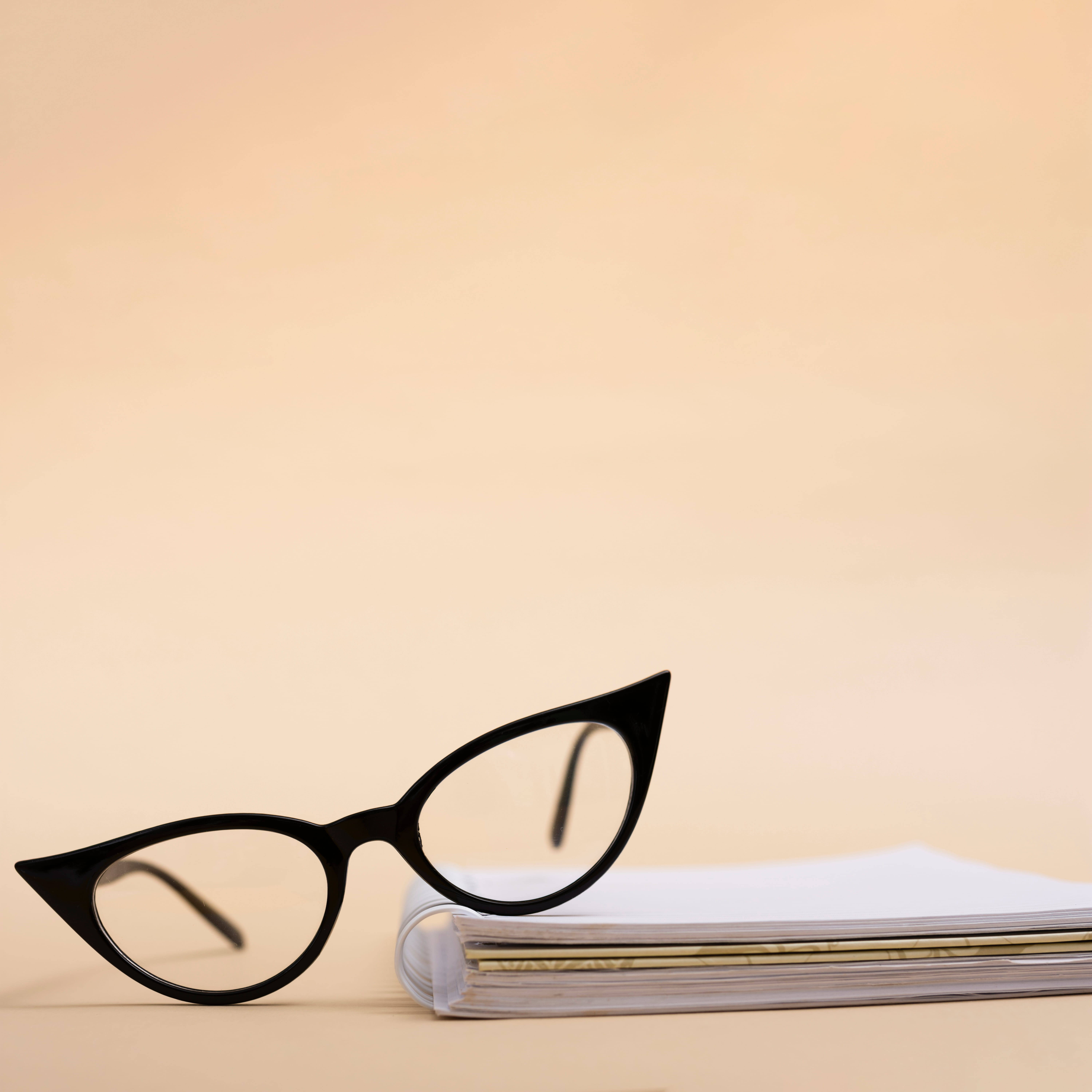 Black cat-eye glasses next to a rolled magazine on beige background