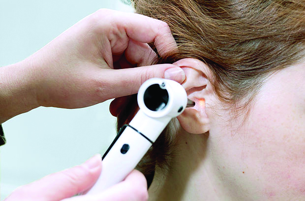 Person using white otoscope to examine inside patient's ear for medical checkup