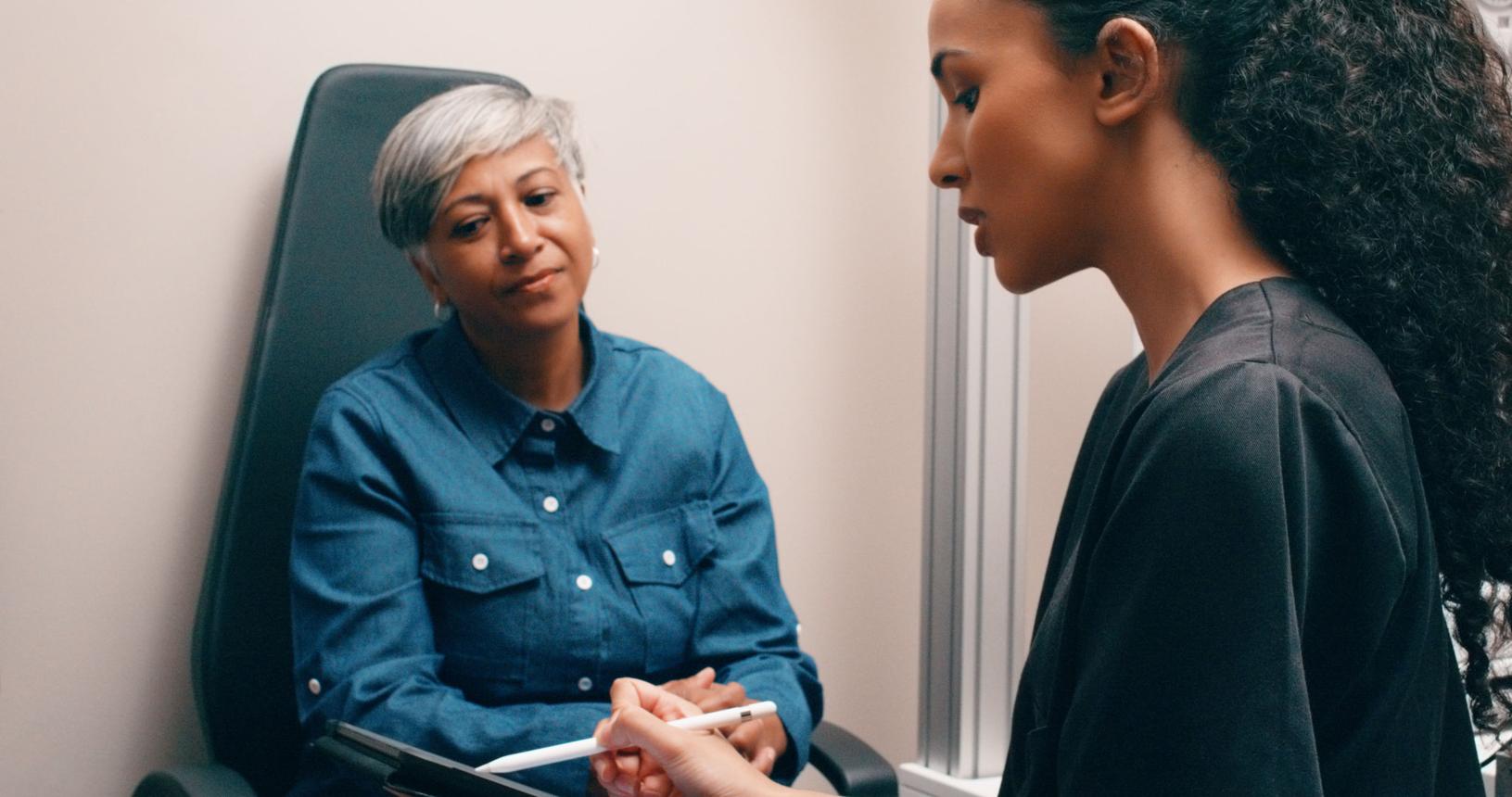 Older woman in denim shirt interviewing or consulting with younger woman holding documents