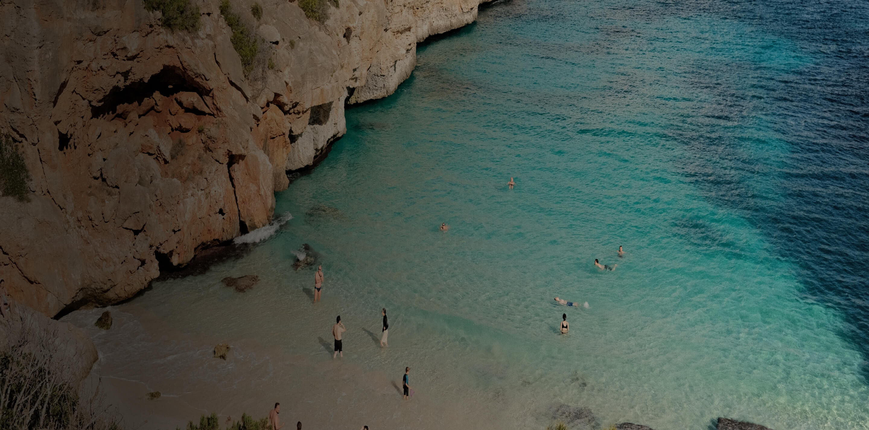 Cliff-edged turquoise Mallorca cove with swimmers in clear water
