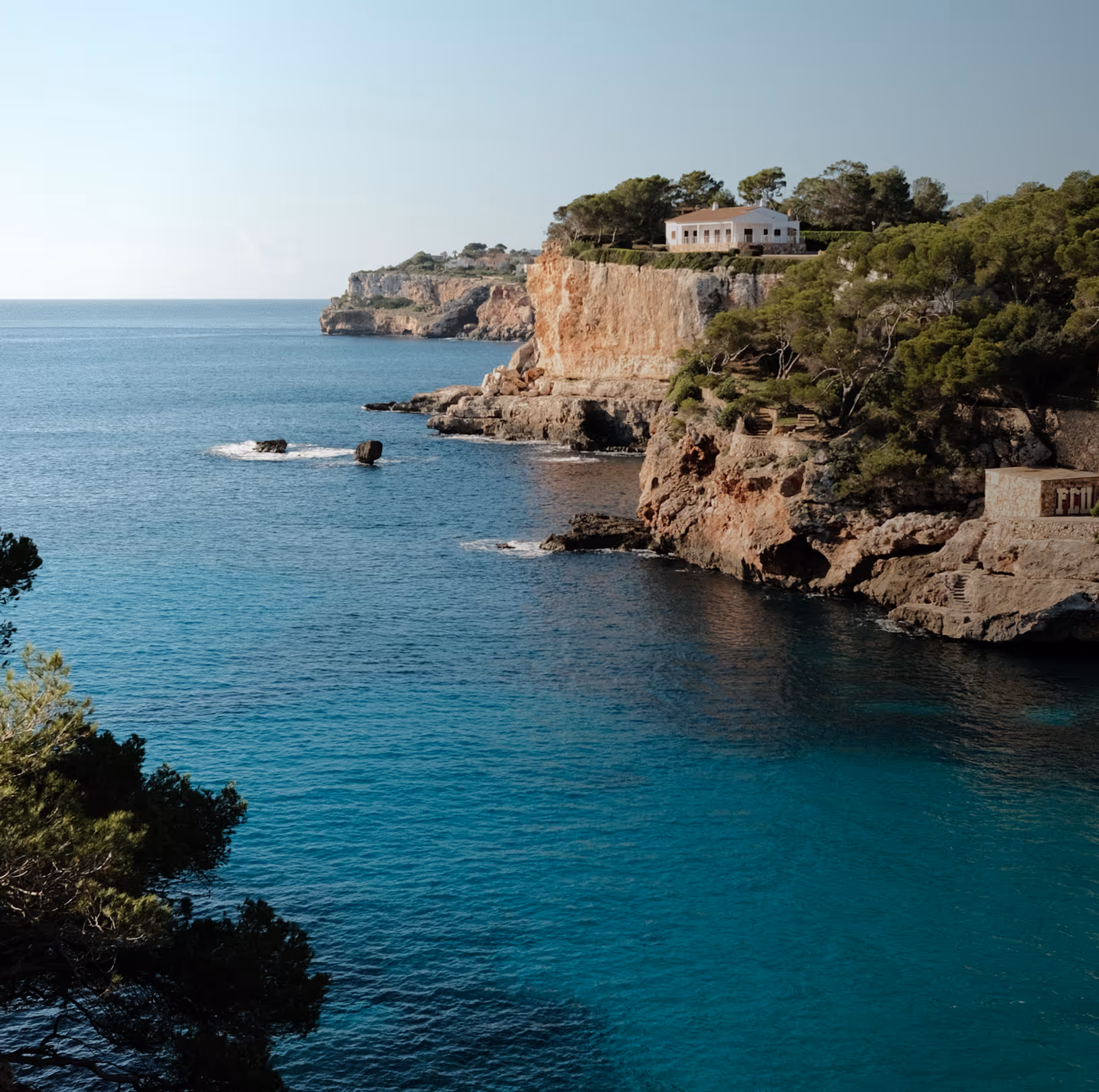 Turquoise cove with pine-clad cliffs and a stone villa on the rocks