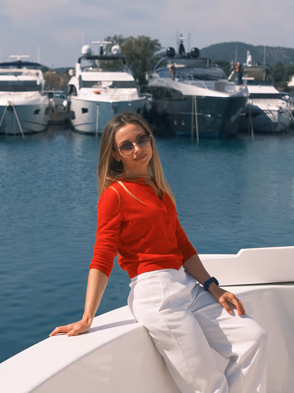 Julia in a red top seated on a yacht in a marina full of boats