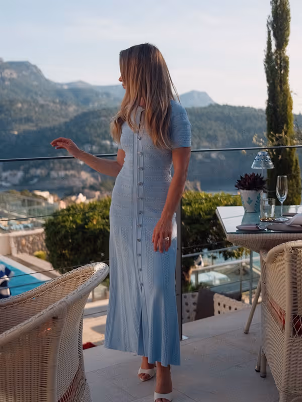 Woman in a pale blue dress on a villa terrace above the sea and mountains