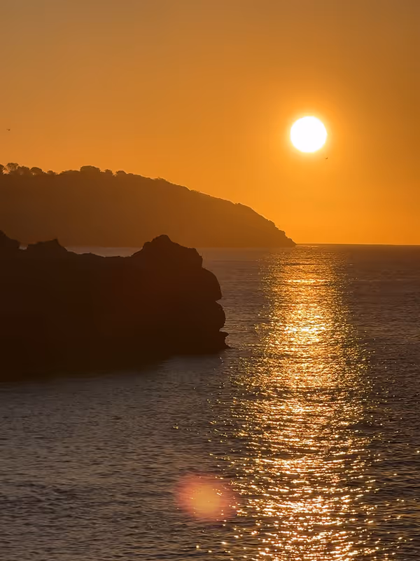 Golden sun setting behind a rocky Mallorca headland over the water